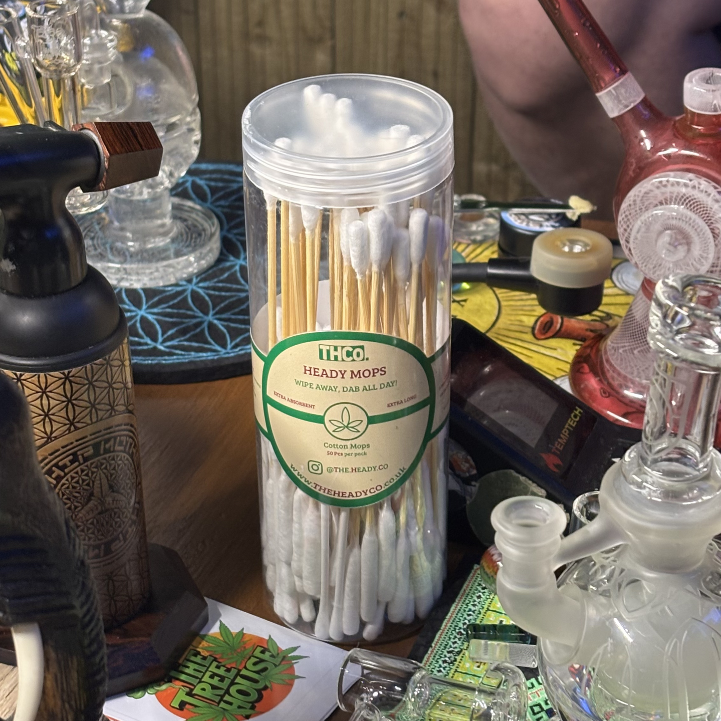 Container of heady mops on a table with various items including glass pipes and a torch