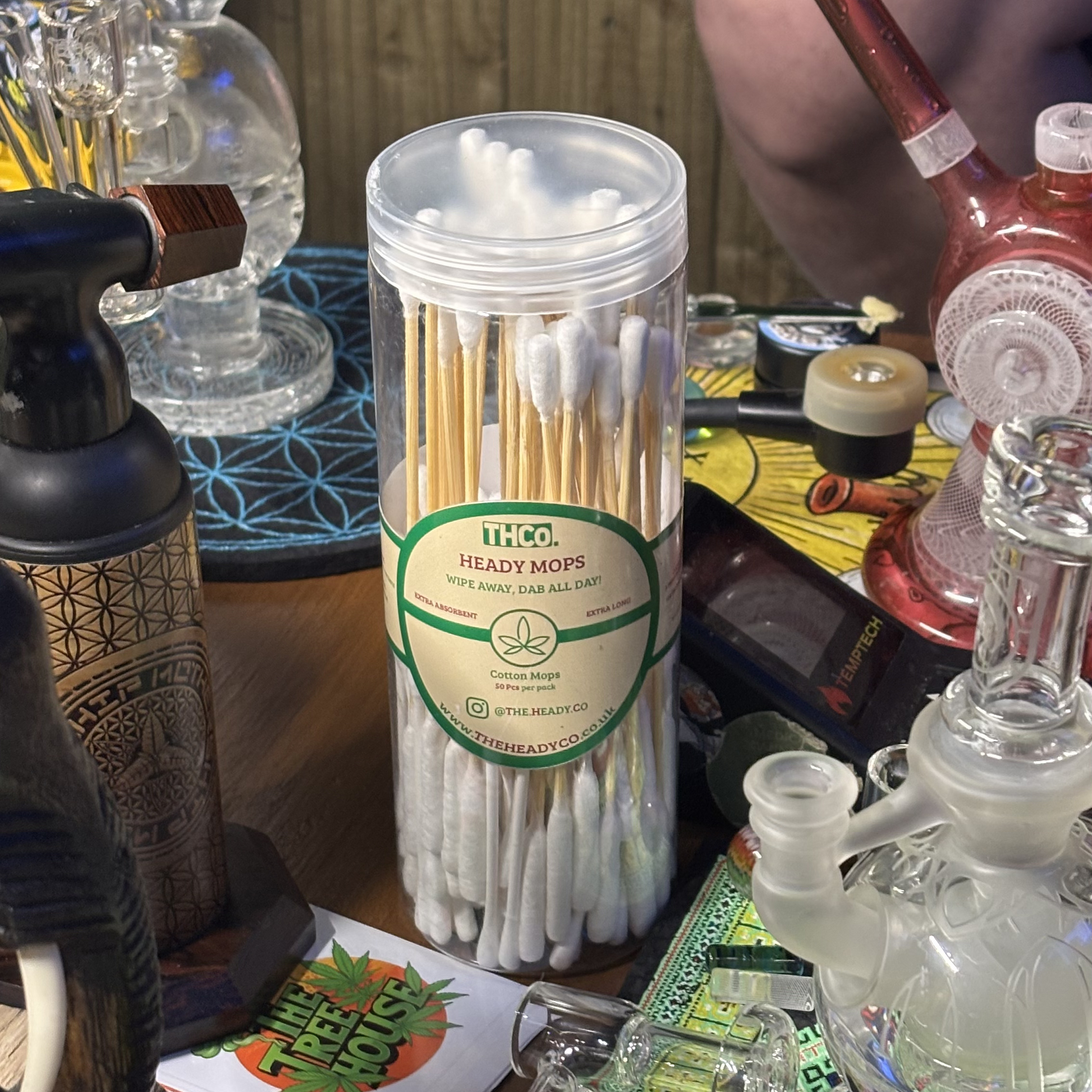 Container of heady mops on a table with various items including glass pipes and a torch