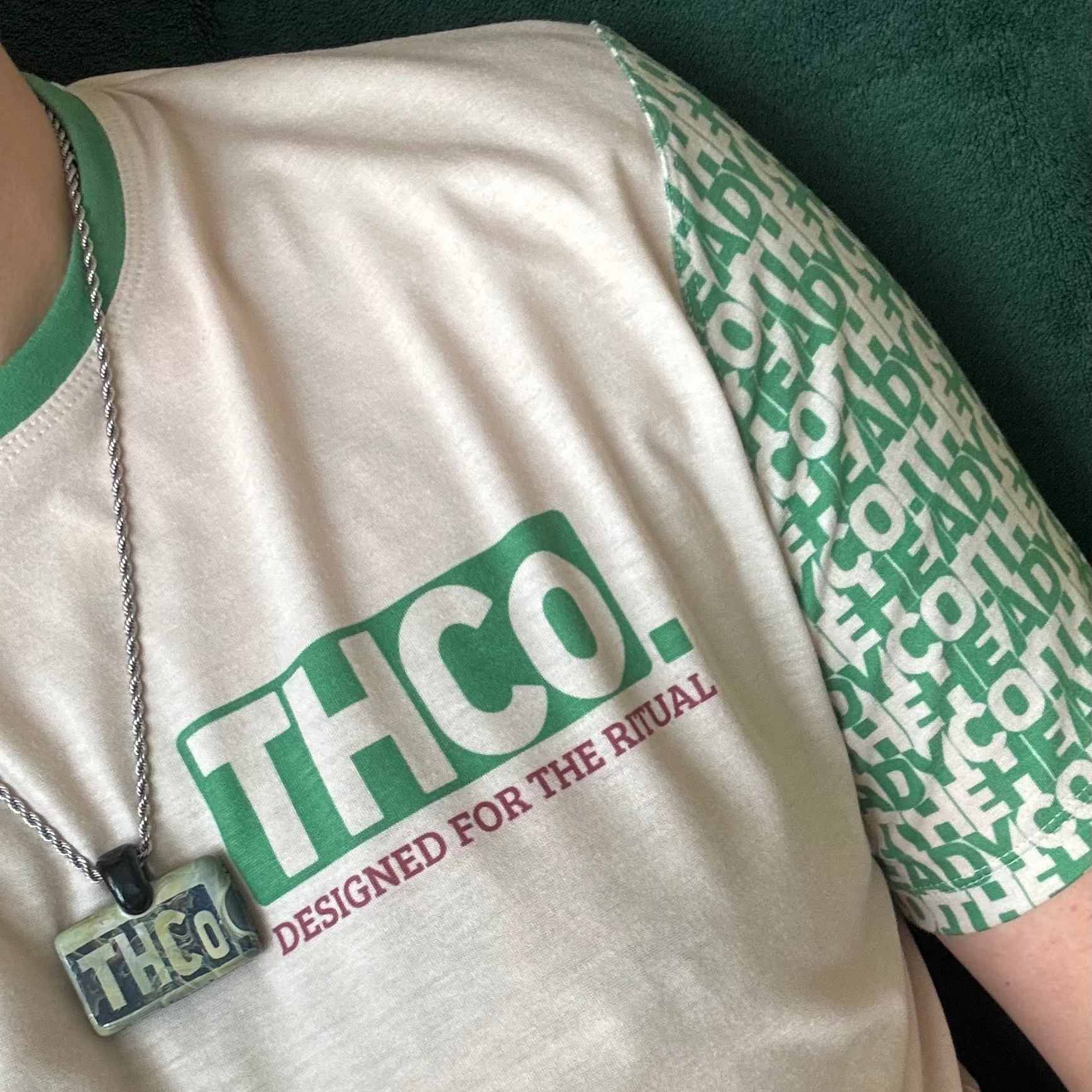 Person wearing a cream and green t-shirt with green and red 'THCO' branding.
